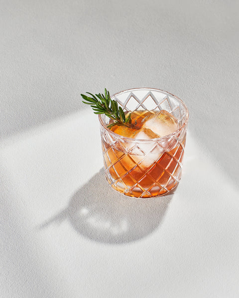 an image of a cocktail with a sprig of herbs and ice in the sunlight
